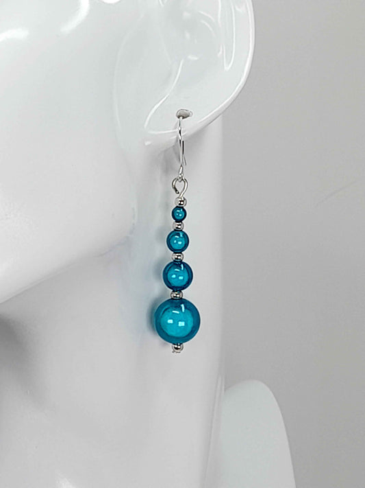 Turquoise blue miracle bead drop earrings with silver plated hooks hanging, on a white mannequin head