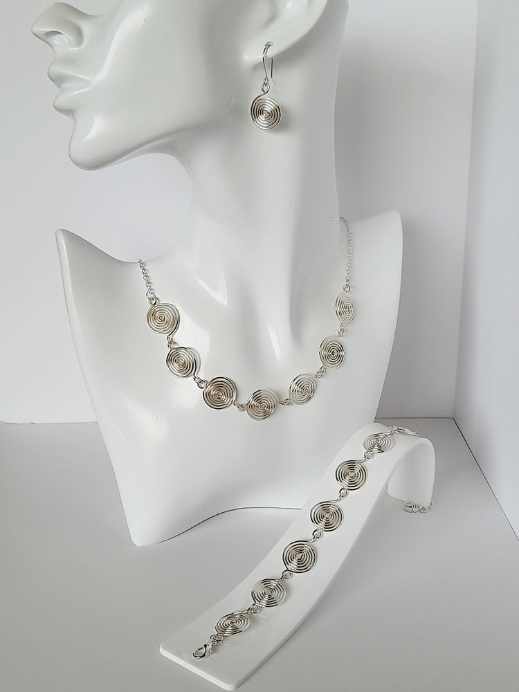 Silver spiral jewellery set featuring handcrafted silver spirals made into drop earrings, necklace and bracelet, shown on a white head mannequin.