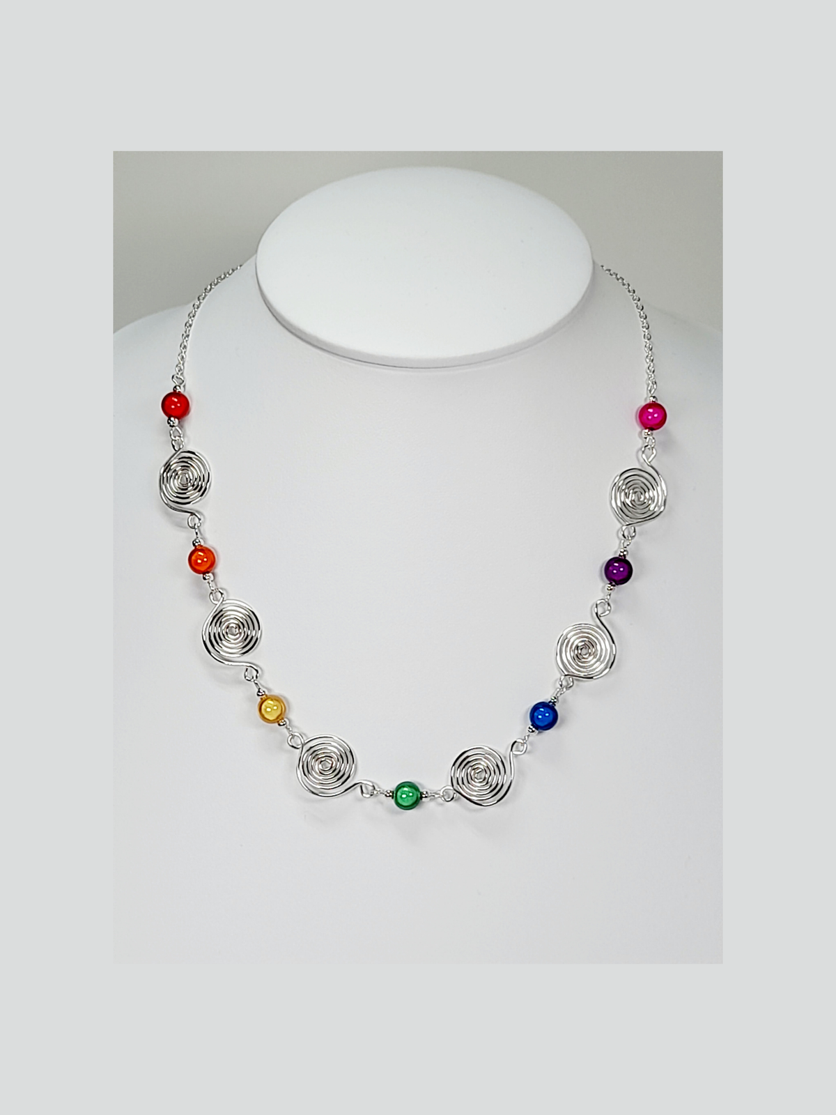 Handmade necklace with alternating rainbow coloured miracle beads alternating with handmade silver spirals, finished with silver plated chain and a silver plated lobster clasp.