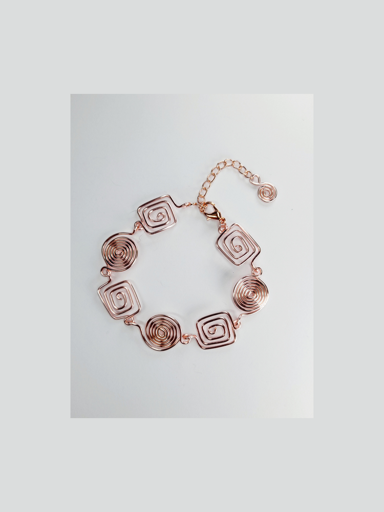 Handmade rose gold bracelet with four square spirals and three round spirals on a white background.