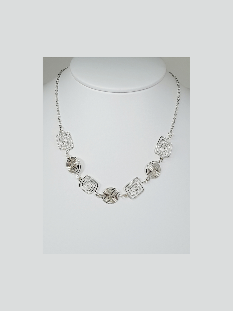 A silver spiral necklaces made of square and round spirals and silver plated chain shown on a white background.