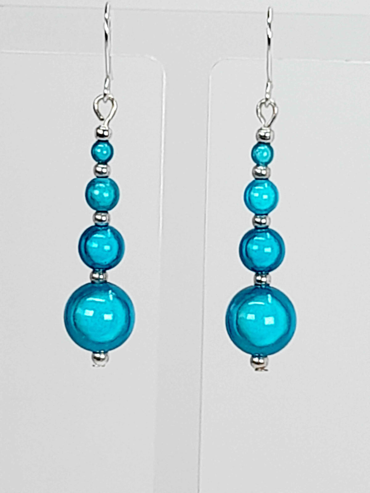 Turquoise blue miracle bead drop earrings with silver plated hooks hanging, with a white background