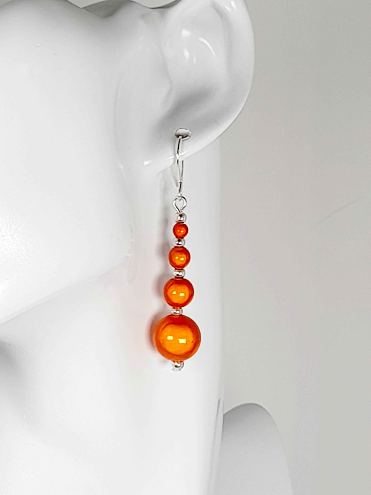 Bright orange miracle bead drop earrings on white mannequin head
