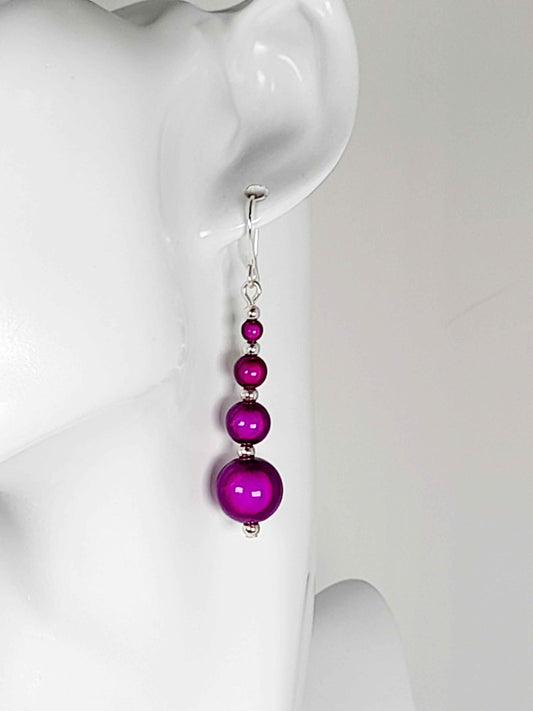Bright purple miracl bead drop earrings on a white manequin.