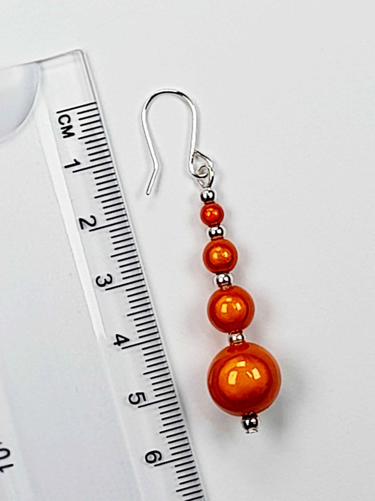 Bright orange miracle bead drop earring with ruler showing 6cm drop