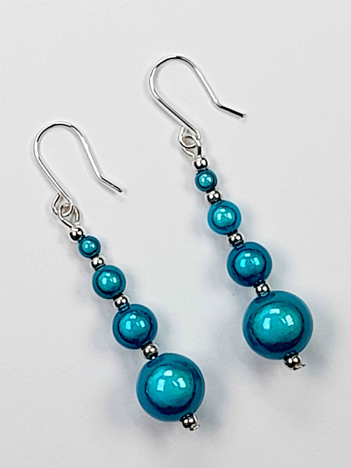 Turquoise blue miracle bead drop earrings with silver plated hooks with a white background