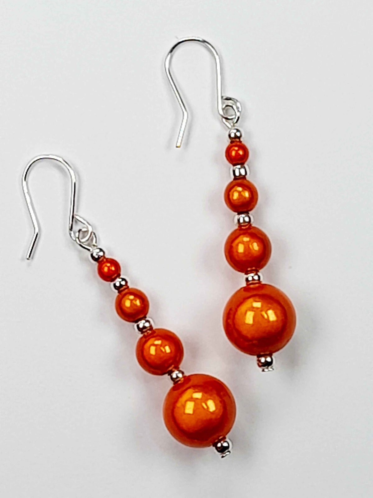 Bright orange miracle bead dangle earrings on white background.