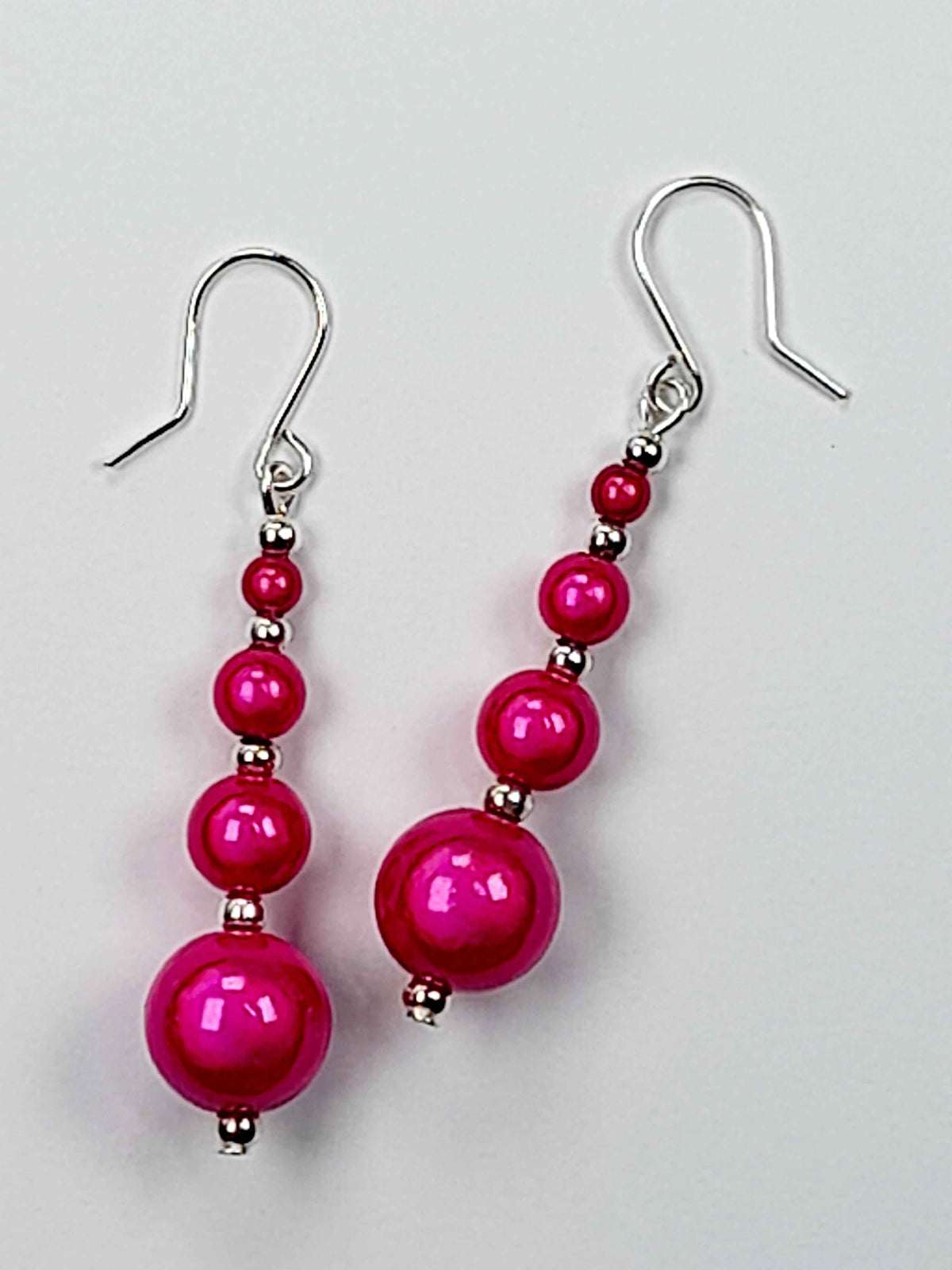 Bright pink miracle bead dangle earrings on a white background.
