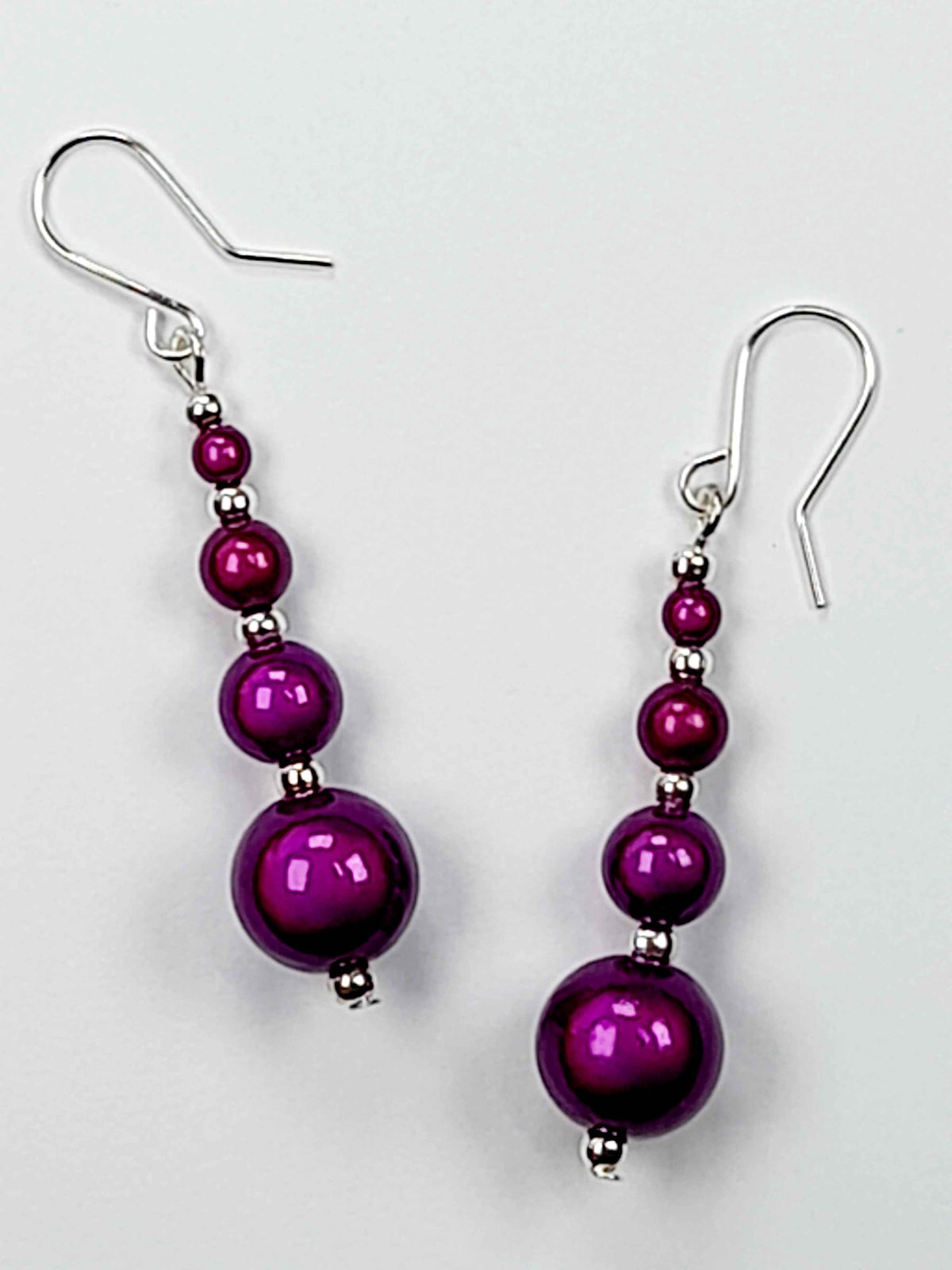 Pair of bright purple miracle bead earrings with silver ear hooks displayed on a white background.